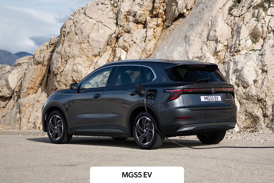A dark grey MGS5 EV parked in front of a rockface